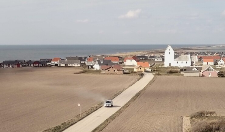 Luftbillede af bil på grusvej med kirke i baggrunden